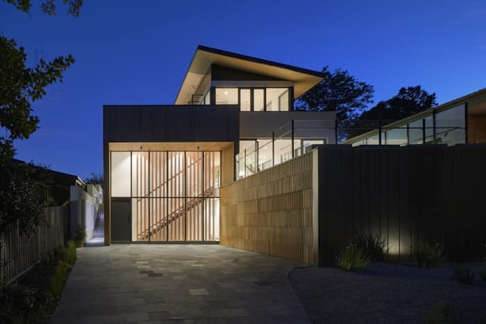 Maison moderne à la nuit tombée avec façade vitrée, escalier éclairé et design contemporain épuré en bois et verre.