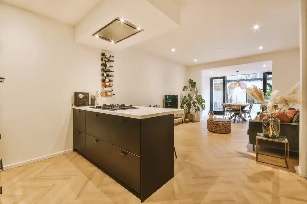 Cuisine ouverte moderne avec îlot noir, parquet en chevrons, salon lumineux et salle à manger contemporaine.