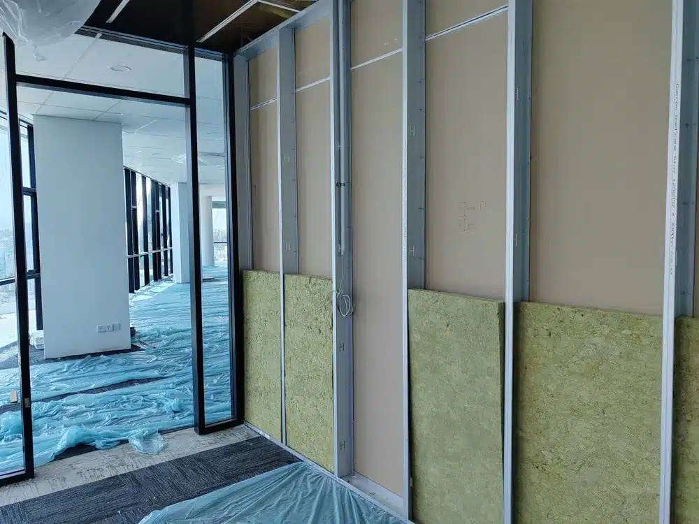Pose d'isolant en laine minérale sur profilés Gypframe lors de l'aménagement d'un bureau moderne en chantier.