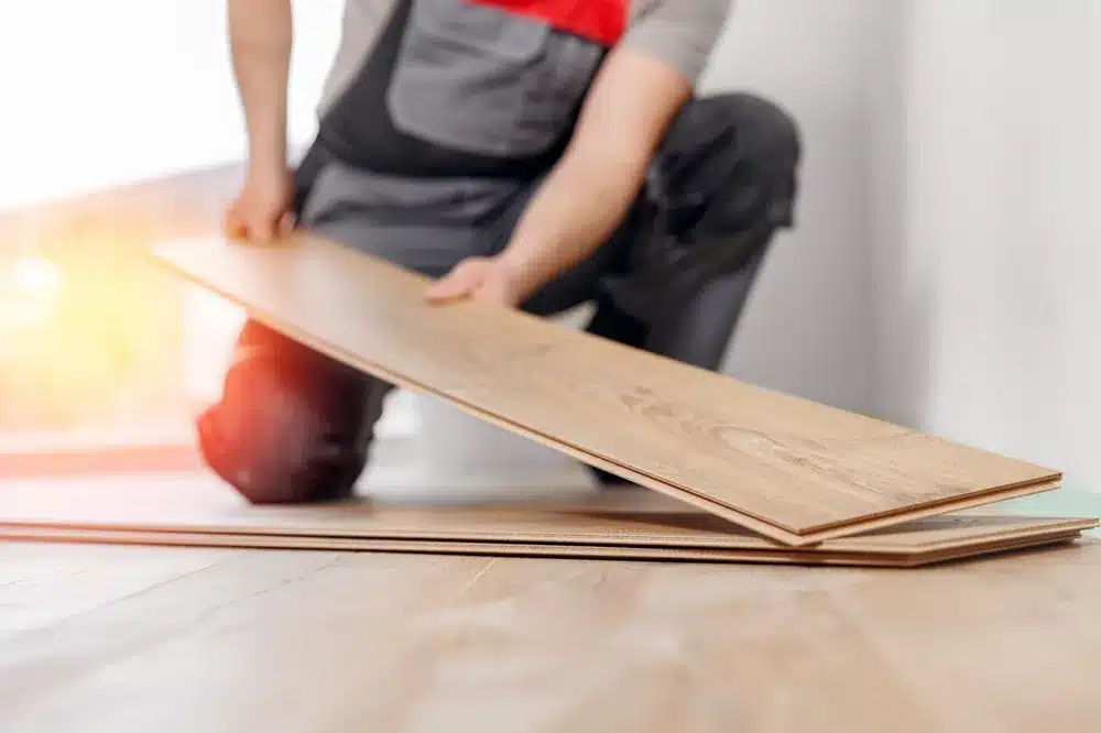 Un artisan installe des lames de parquet stratifié au sol d'une pièce lumineuse, geste précis et professionnel.